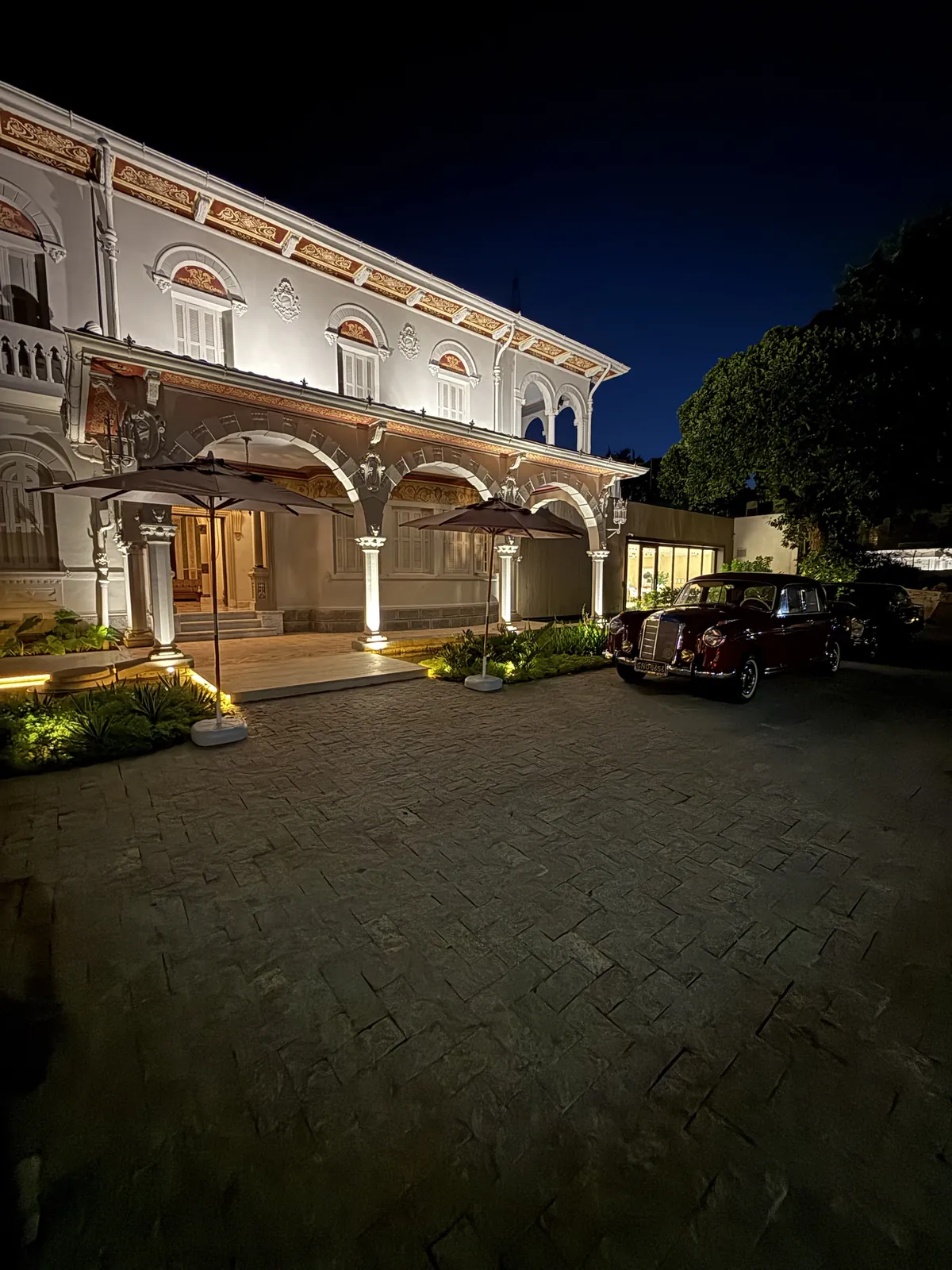 Fachada do casarão iluminada à noite, com os guarda-sóis recolhidos e o Ponton bordô no pátio.